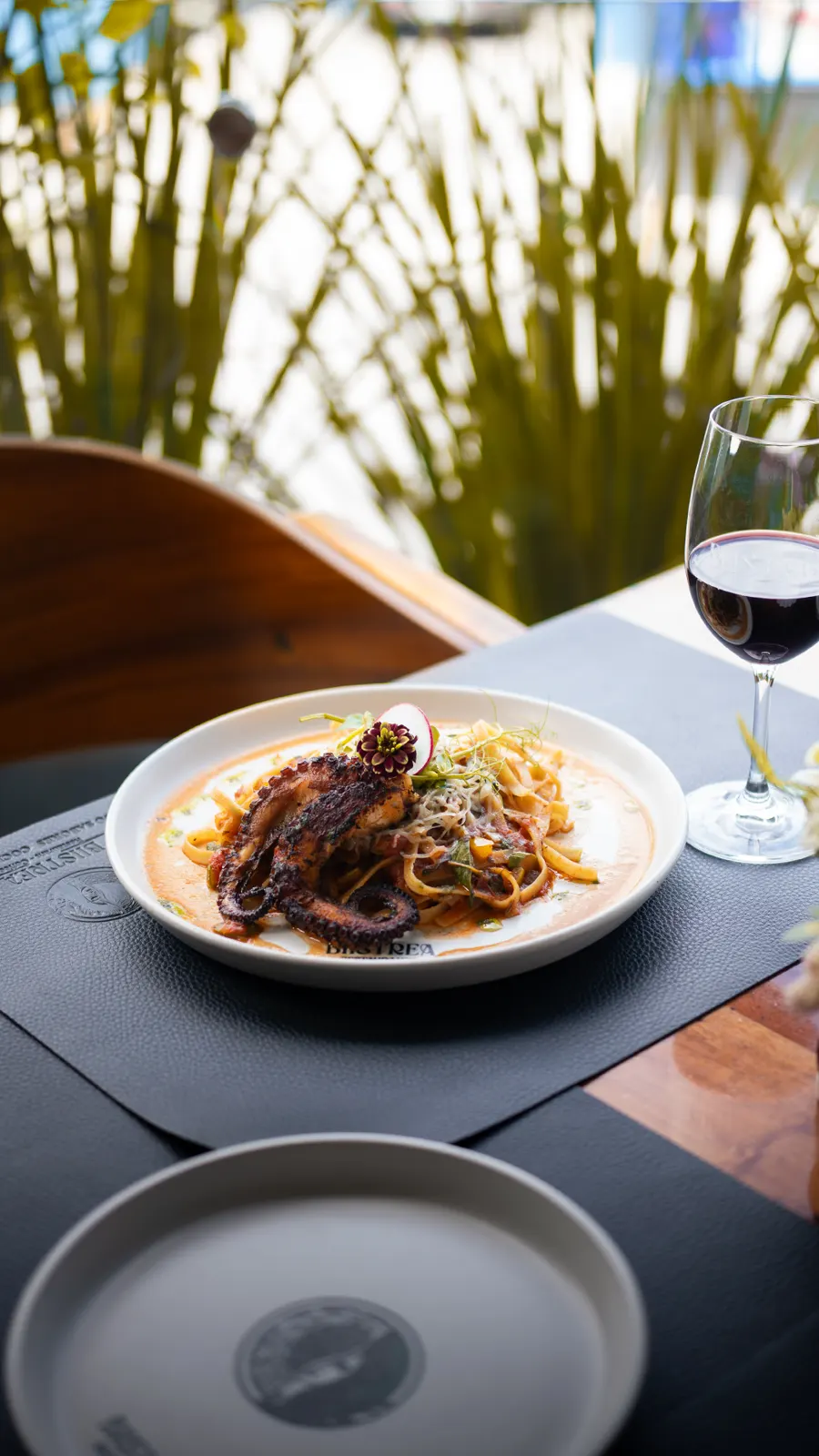 Pasta con pulpo y una copa de vino tinto sobre la mesa