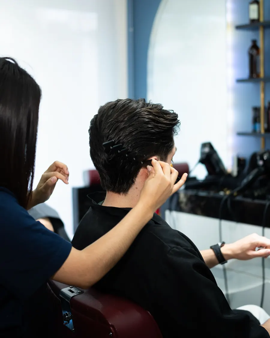 Estilista peinando a un cliente sentado en un sillón de barbería
