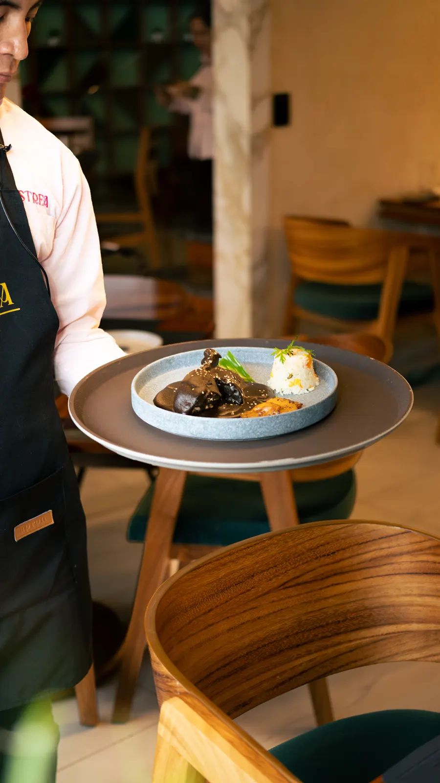 Mesero llevando un platillo en una charola dentro de un restaurante